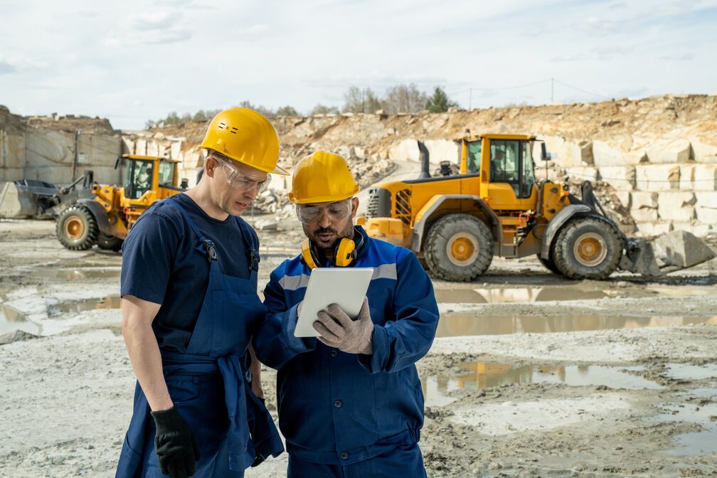 two male workers at construction site collaborate using mobile computer